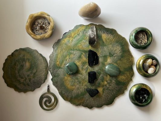 Handmade green and gold resin catch-all tray with Capricorn ritual crystals including black tourmaline, smoky quartz, and green aventurine, surrounded by resin tiny bowls filled with herbs and stones, spiral pendant, and incense holder on white background
