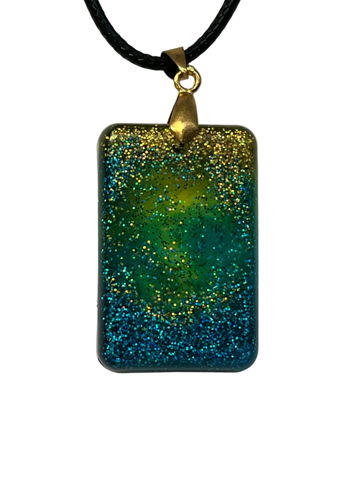 Handcrafted rounded rectangle resin pendant with chartreuse yellow fading into teal and deep blue, covered in dense multidimensional holographic glitter, suspended from a black braided cord with a gold-toned bail.