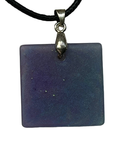 Handcrafted square resin pendant with swirling lavender, periwinkle, and steel blue shimmer and scattered gold and green glitter flecks, suspended from a black braided cord with a silver-toned bail.