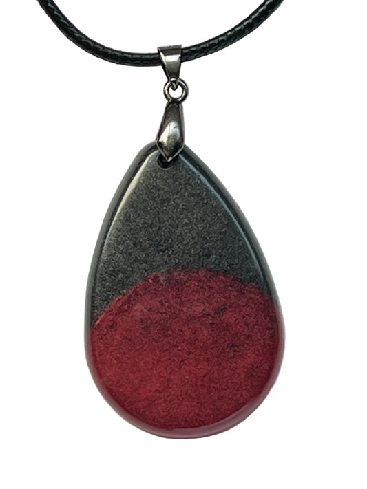 Handcrafted teardrop resin pendant with charcoal black holographic shimmer on the upper half and rich crimson red on the lower half in a bold two-tone colorblock design, suspended from a black braided cord with a silver-toned bail.