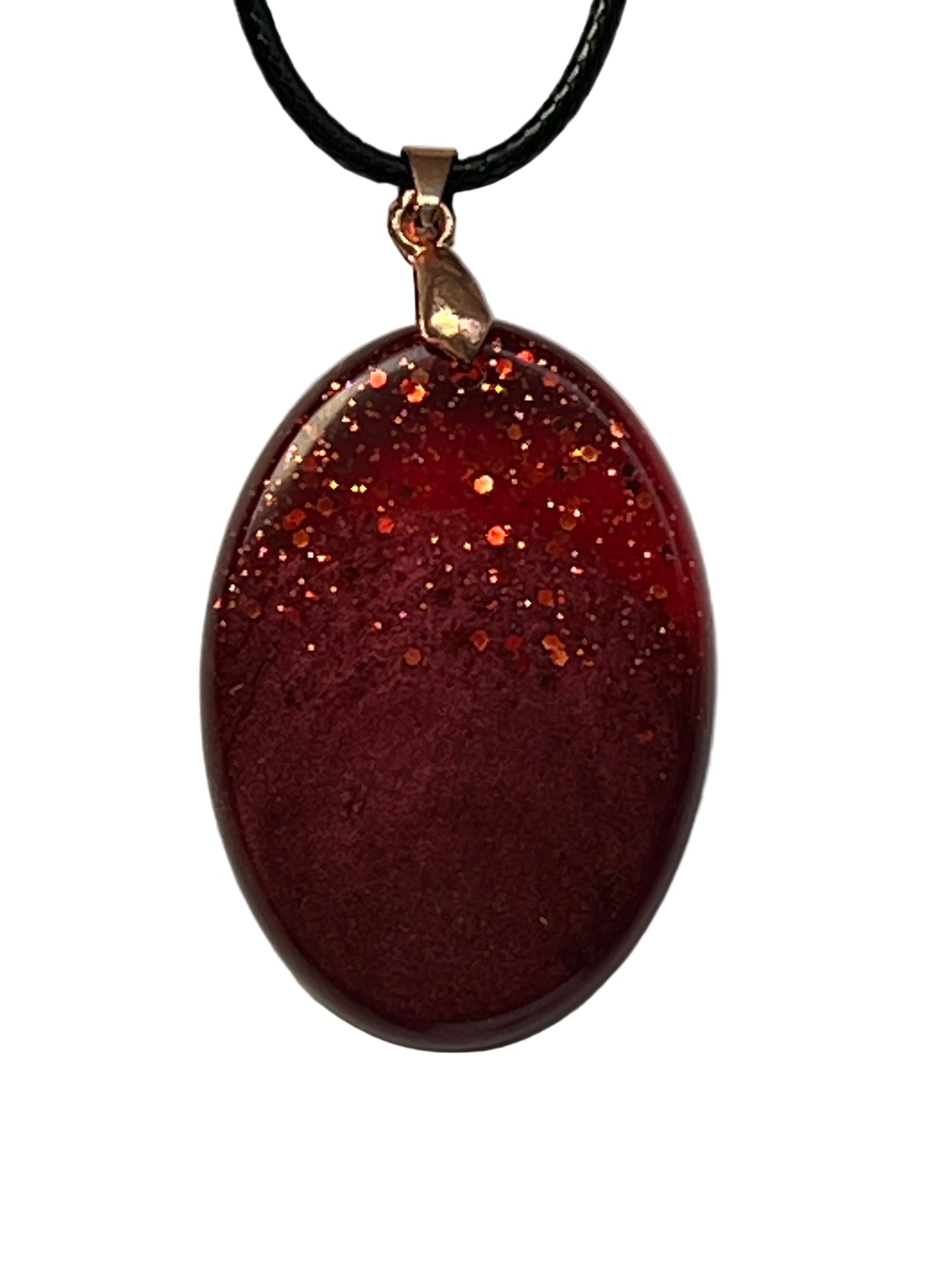 Handcrafted deep burgundy red resin oval pendant with scattered copper and orange glitter in the upper portion fading into a rich velvety matte base, suspended from a black braided cord with a copper-toned bail.
