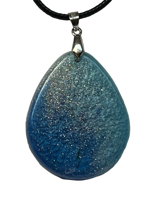 Handcrafted deep blue resin teardrop pendant with layered slate and cobalt tones and dense holographic silver glitter throughout, suspended from a black braided cord with a silver-toned bail.