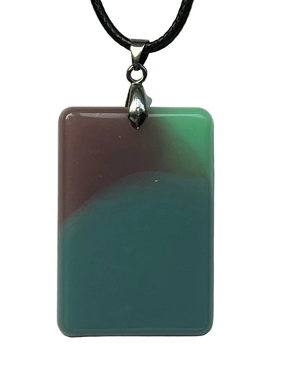 Handcrafted resin rounded rectangle pendant with warm mauve and sage green in the upper portion flowing into deep teal below, with a milky opaque finish, suspended from a black braided cord with a silver-toned bail.