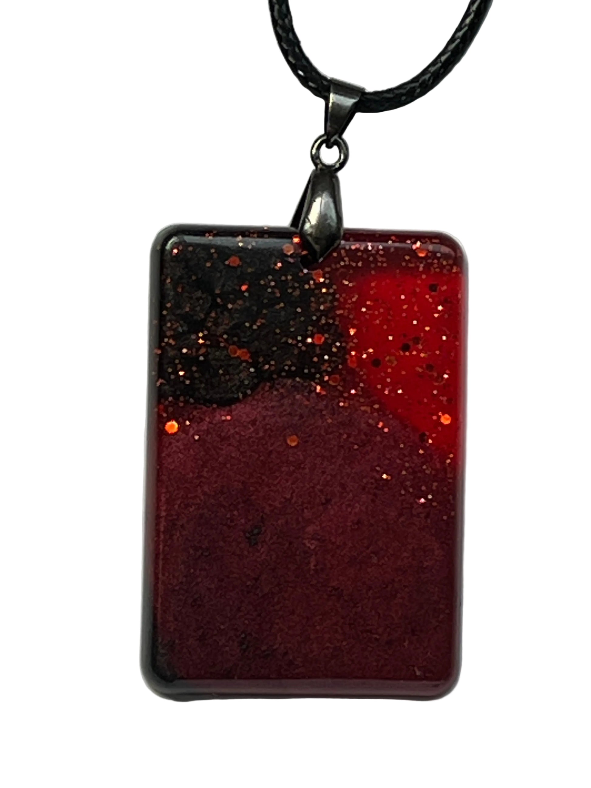 Handcrafted resin rounded rectangle pendant with deep burgundy base, black and crimson red upper tones, and scattered copper and orange glitter throughout, suspended from a black braided cord with a gunmetal bail.