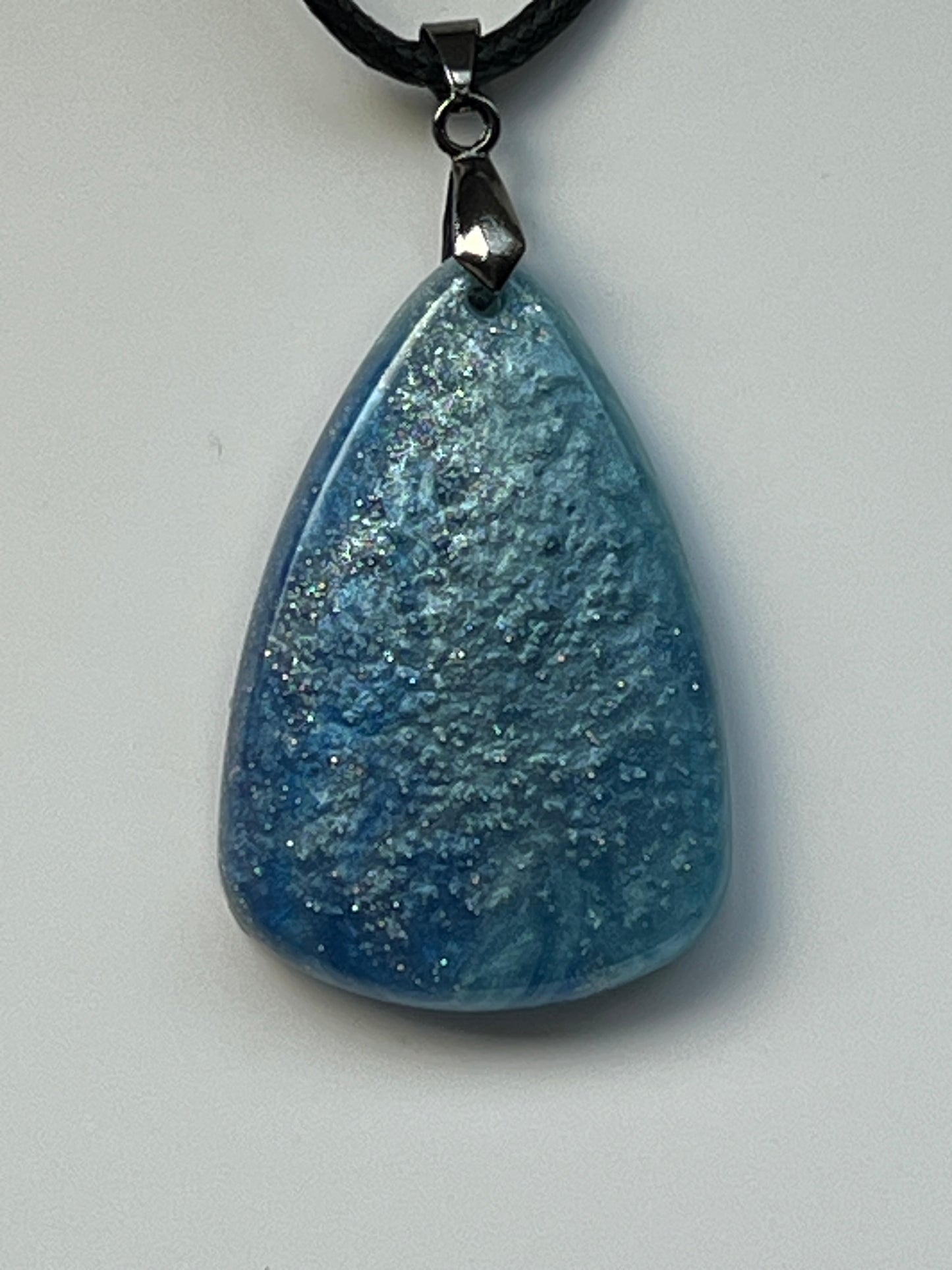 Handcrafted steel blue and dove grey resin wide teardrop pendant with organic cloud-like texture and scattered silver iridescent glitter throughout, suspended from a black braided cord with a gunmetal bail.