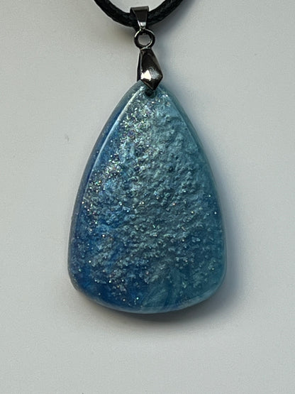 Handcrafted steel blue and dove grey resin wide teardrop pendant with organic cloud-like texture and scattered silver iridescent glitter throughout, suspended from a black braided cord with a gunmetal bail.