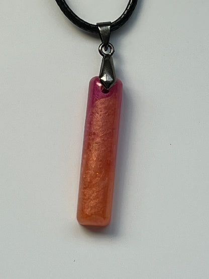 Handcrafted resin elongated bar pendant with warm peach and coral golden shimmer body fading into vivid magenta and hot pink at the top, suspended from a black braided cord with a gunmetal bail.