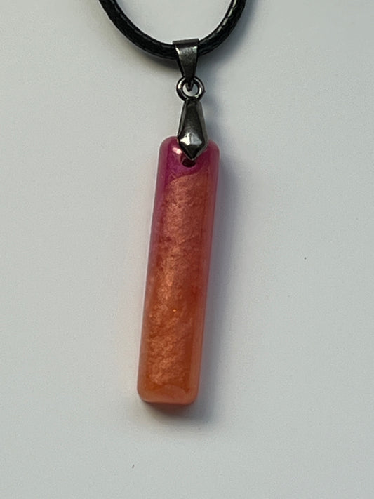 Handcrafted resin elongated bar pendant with warm peach and coral golden shimmer body fading into vivid magenta and hot pink at the top, suspended from a black braided cord with a gunmetal bail.