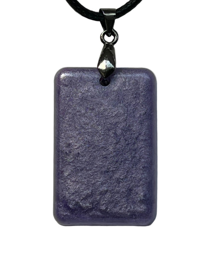 Handcrafted deep dusty violet resin rounded rectangle pendant with subtle matte mineral texture, suspended from a black braided cord with a gunmetal bail.
