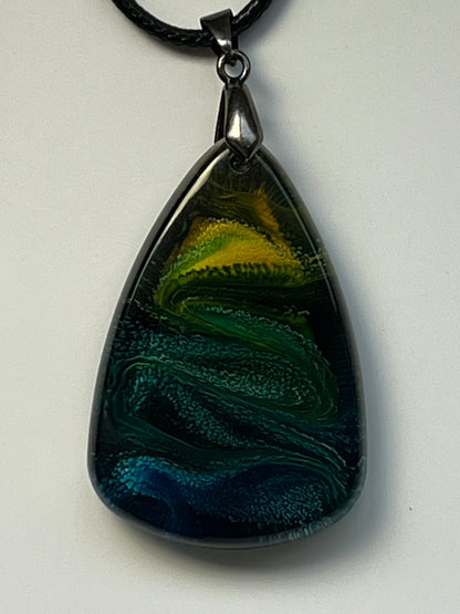 Handcrafted resin teardrop pendant with deep midnight navy and black base, sweeping teal and forest green wave texture, and a glowing electric yellow and chartreuse crown, suspended from a black braided cord with a gunmetal bail.