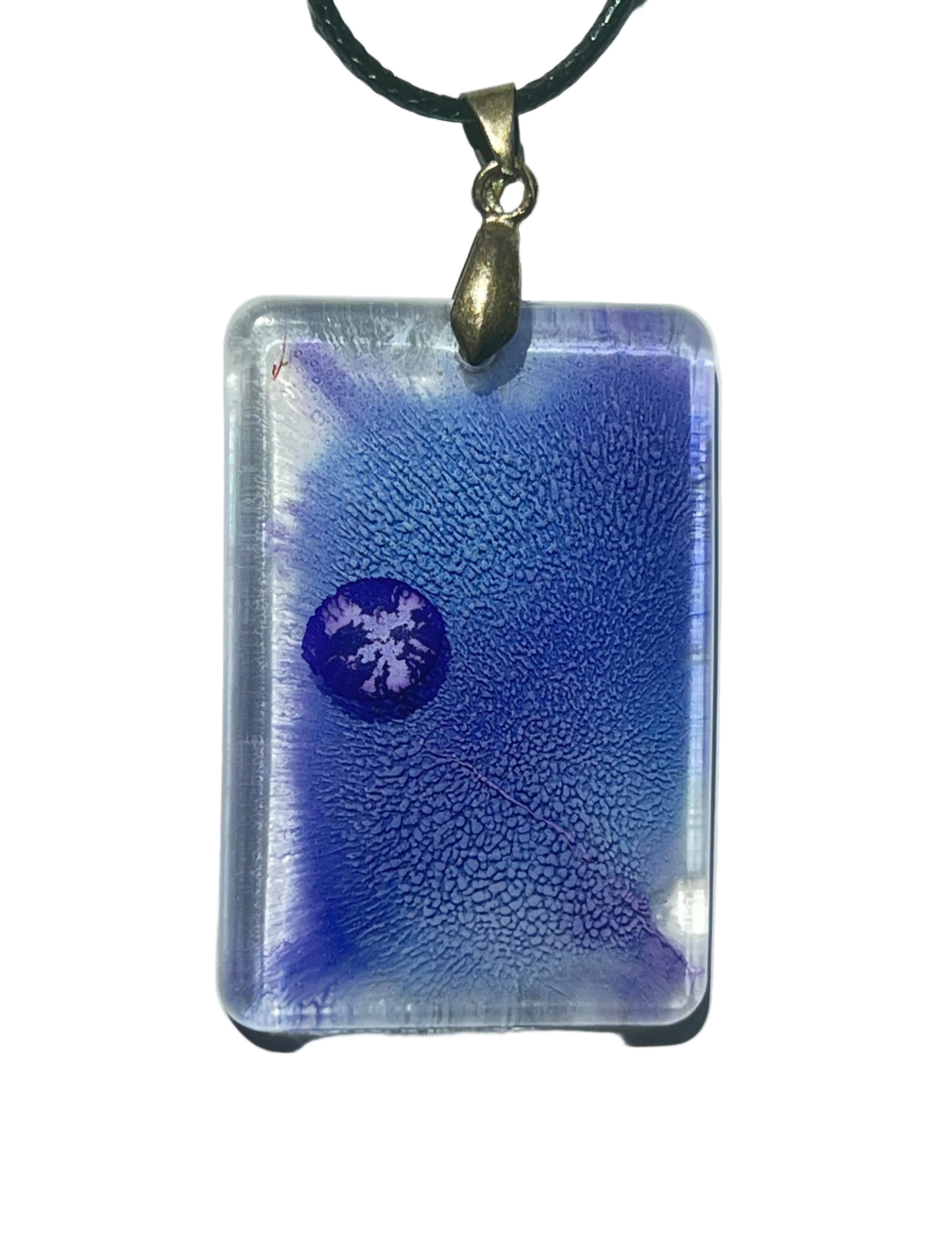 Handcrafted resin rounded rectangle pendant with rich periwinkle and violet fine organic texture, a deep violet moon orb suspended within the field, and luminous crystal-clear edges, suspended from a black braided cord with an antique bronze bail.