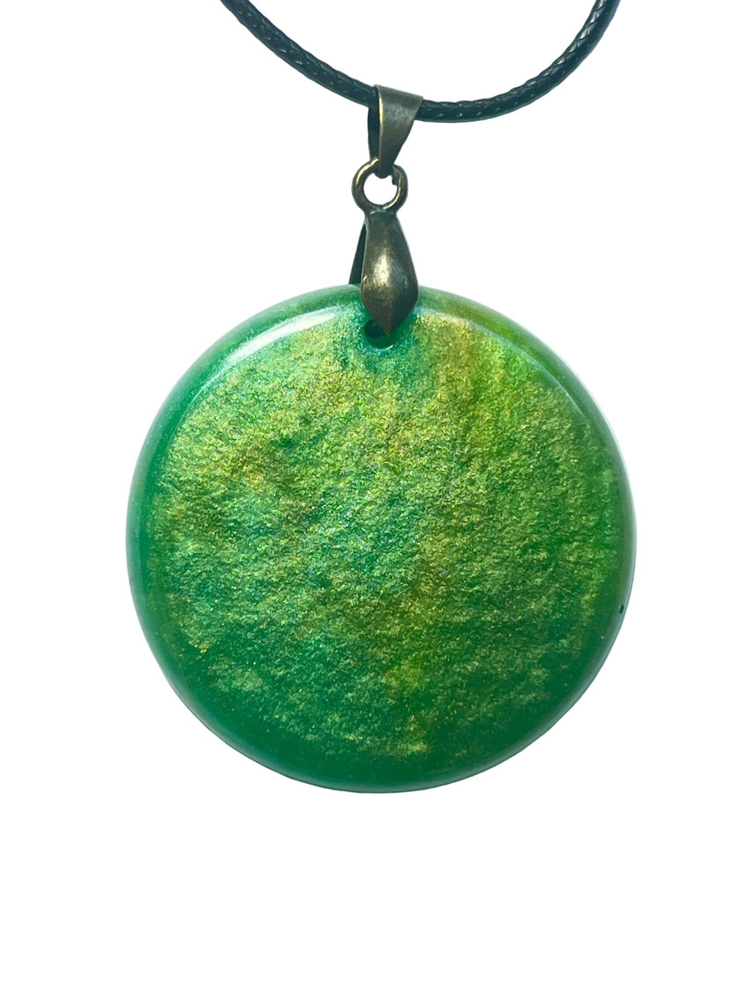 Handcrafted rich emerald green resin large circle pendant with swirling warm gold shimmer throughout and a domed luminous surface, suspended from a black braided cord with an antique bronze bail.
