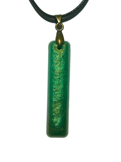 Handcrafted emerald green resin bar pendant with a warm gold shimmer ribbon running through the center, suspended from a black braided cord with an antique bronze bail.