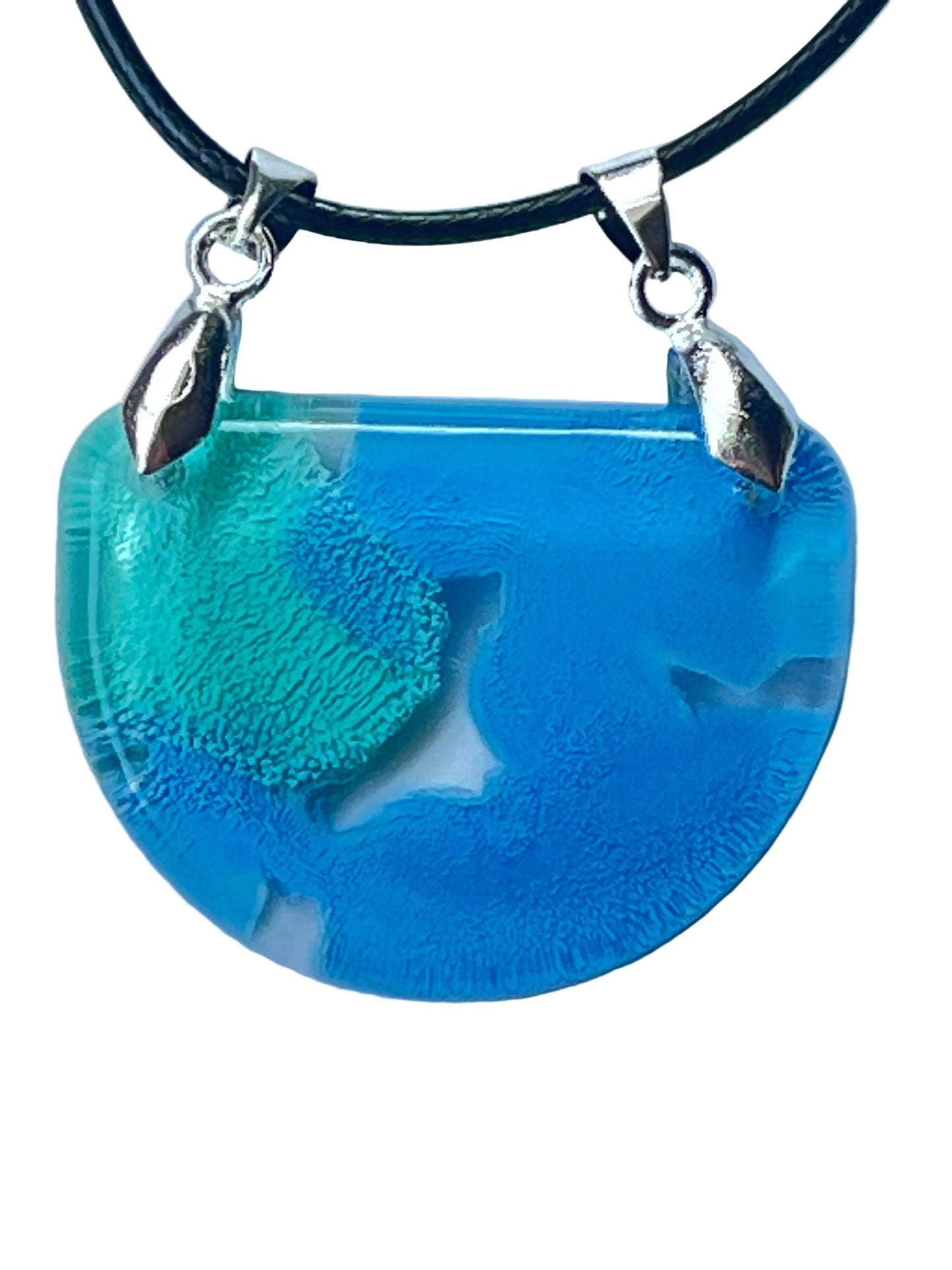 Handcrafted resin half moon pendant with vivid sky blue field and a bold teal and seafoam green organic island-like form with fine horizontal texture and glassy translucent qualities, suspended from a black braided cord with dual silver-toned bails.