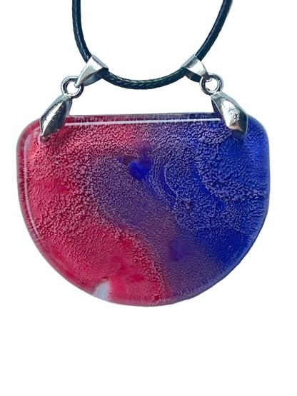 Handcrafted resin half moon pendant with warm rose and crimson on the left sweeping into deep cobalt and royal blue on the right with a blue-violet vortex at center and fine cellular texture throughout, suspended from a black braided cord with dual silver-toned bails.
