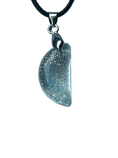 Handcrafted crystal clear resin domed half moon pendant with dense fine silver glitter throughout and a cluster of clear iridescent bubble inclusions, suspended from a black braided cord with a silver-toned bail.