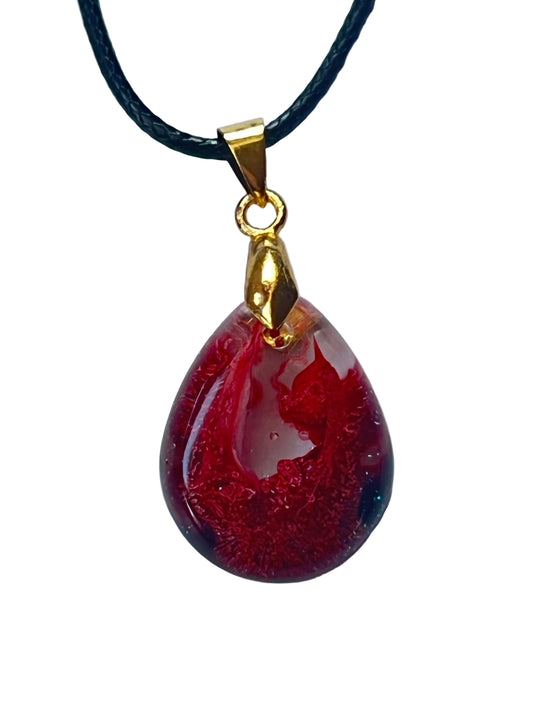 Handcrafted deep jewel-toned crimson and ruby red resin glassy domed teardrop pendant with extraordinary fine cellular interior texture and translucent glowing edges, suspended from a black braided cord with a gold-toned bail.