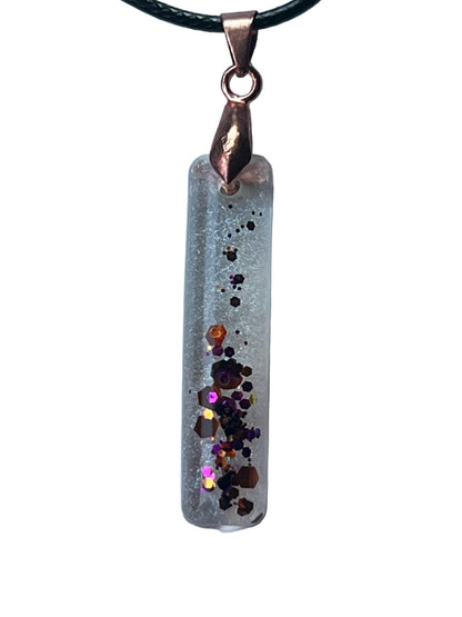 Handcrafted crystal clear resin elongated bar pendant with white frost texture and a central cascade of chunky burgundy, black, violet, magenta, and copper glitter, suspended from a dark braided cord with a copper-toned bail.