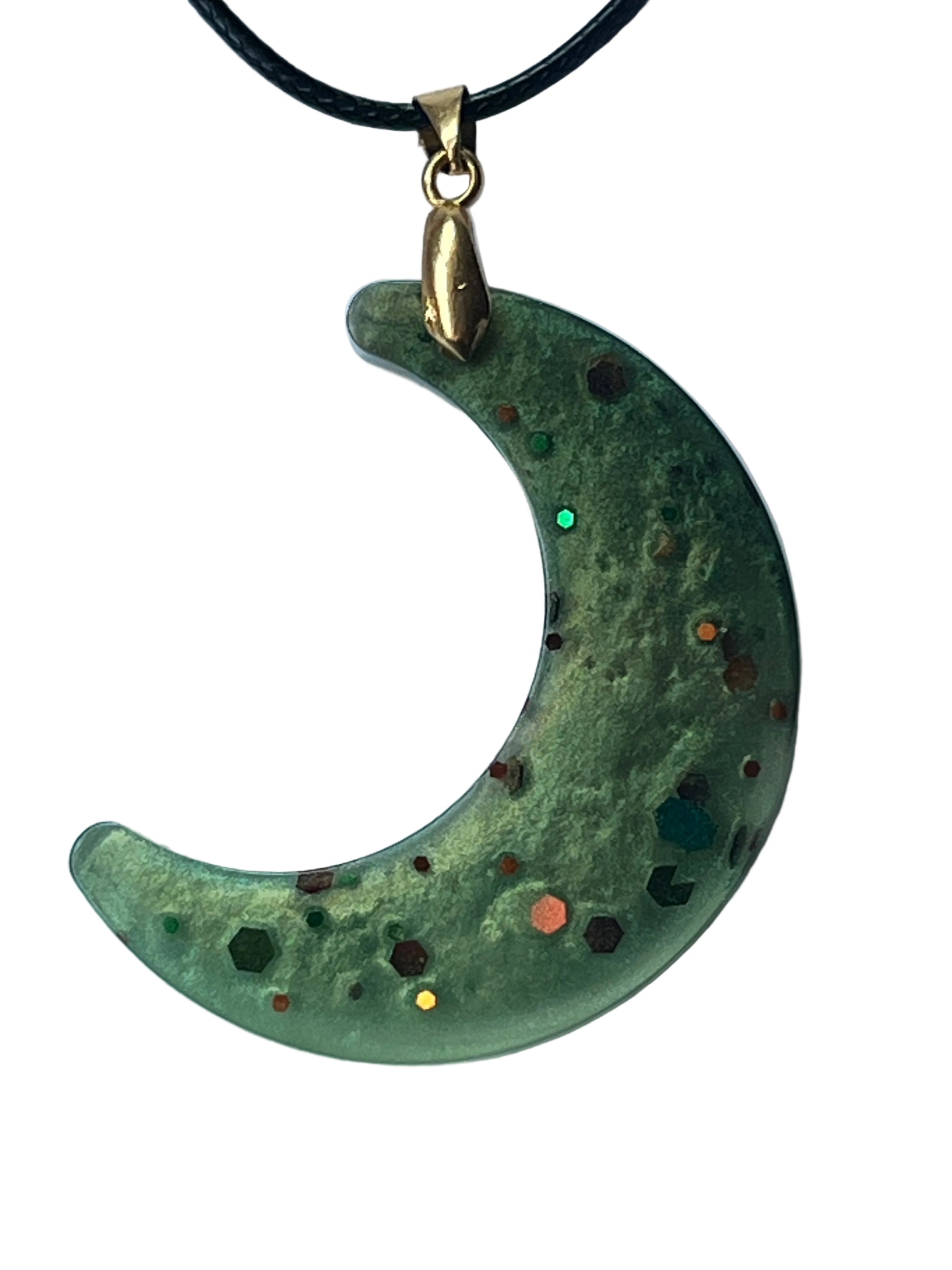 Handcrafted rich moss and sage green resin crescent moon pendant with mottled organic texture and scattered chunky hexagonal confetti in teal, copper, orange, burgundy, and gold, suspended from a black braided cord with a gold-toned bail.