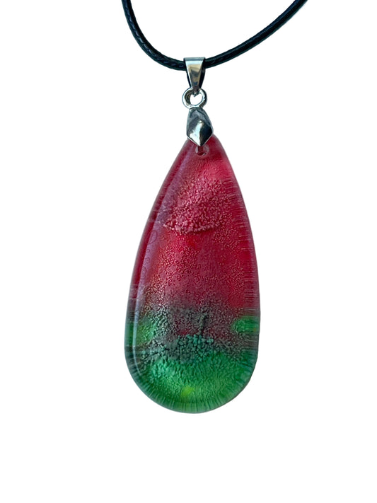 Handcrafted resin elongated teardrop pendant with translucent coral and rose red upper field fading to vivid emerald green base with fine horizontal texture and glassy gemstone-like luminosity, suspended from a black braided cord with a silver-toned bail.