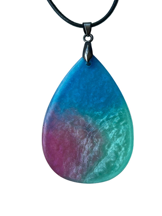Handcrafted large resin teardrop pendant with vivid sky blue upper field, deep magenta-rose lower left, and luminous pearlescent mint lower right blending into a swirling mauve center, with a rich atmospheric matte-to-satin finish, suspended from a black braided cord with a gunmetal bail.