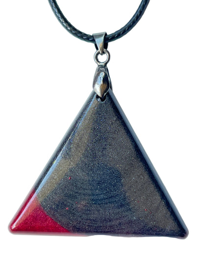Handcrafted deep midnight black resin large triangle pendant with fine dark shimmer throughout and a bold glossy crimson red triangle accent at the lower left corner, suspended from a black braided cord with a gunmetal bail.