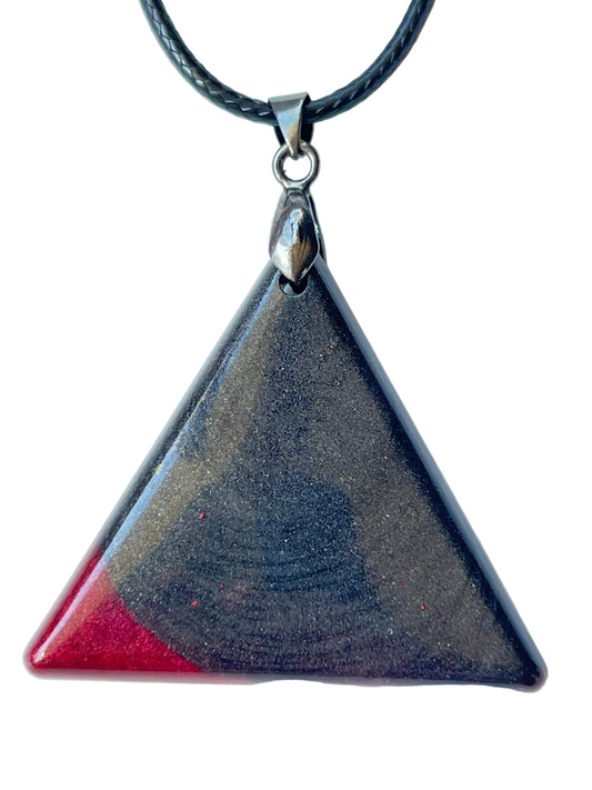 Handcrafted deep midnight black resin large triangle pendant with fine dark shimmer throughout and a bold glossy crimson red triangle accent at the lower left corner, suspended from a black braided cord with a gunmetal bail.