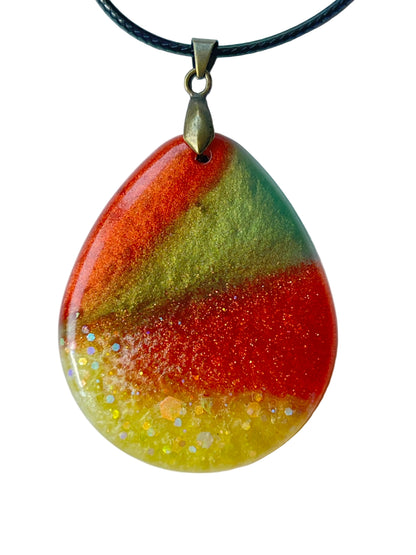 Handcrafted resin wide teardrop pendant with deep forest and olive green upper tones sweeping into warm rust and burnt sienna with a luminous chartreuse gold holographic glitter base, suspended from a black braided cord with an antique bronze bail.