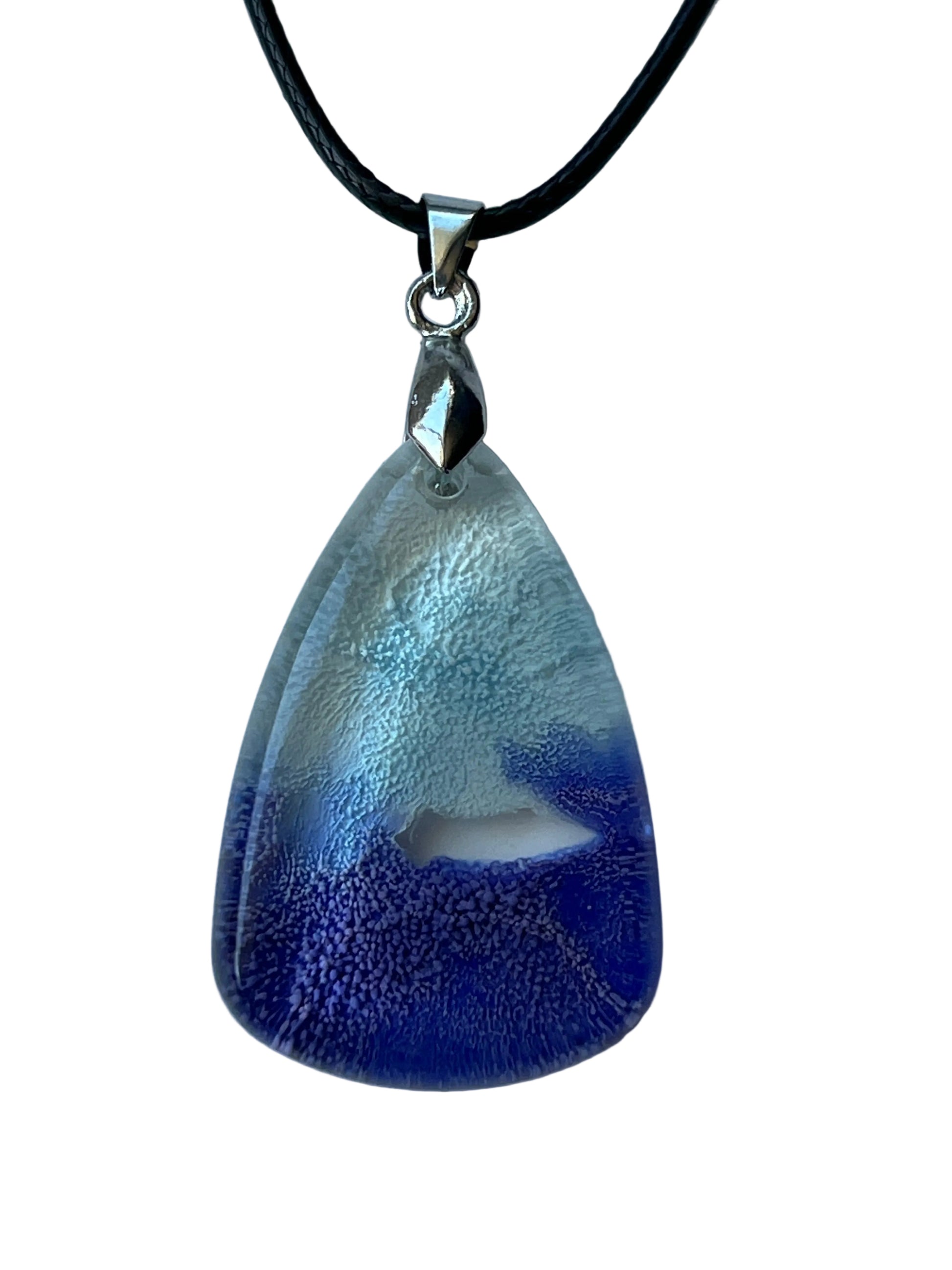 Handcrafted resin wide teardrop pendant with pale silver-white frost upper field and rich indigo deep blue lower field meeting in a dramatic organic cloud-like boundary with fine cellular texture throughout, suspended from a black braided cord with a silver-toned bail.