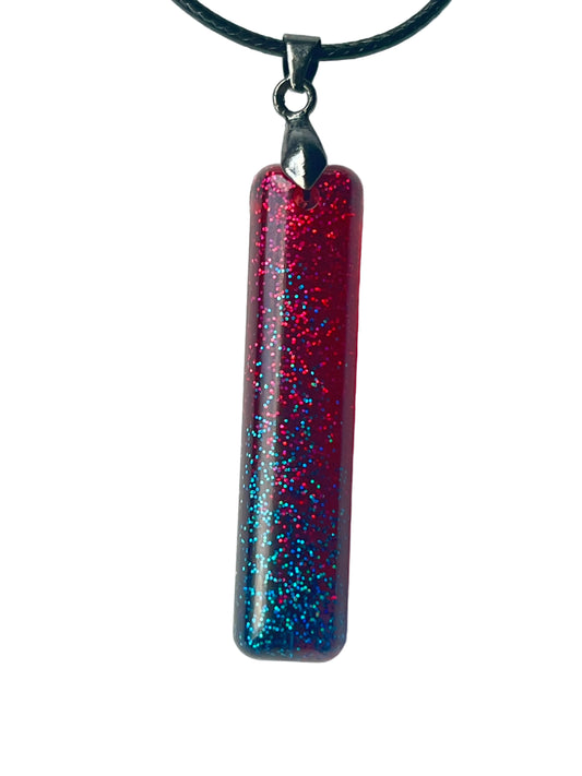 Handcrafted deep translucent crimson resin tall rectangular bar pendant with dense fine glitter shifting from hot magenta-red in the upper field to vivid teal and electric blue in the lower half, suspended from a black braided cord with a gunmetal bail.
