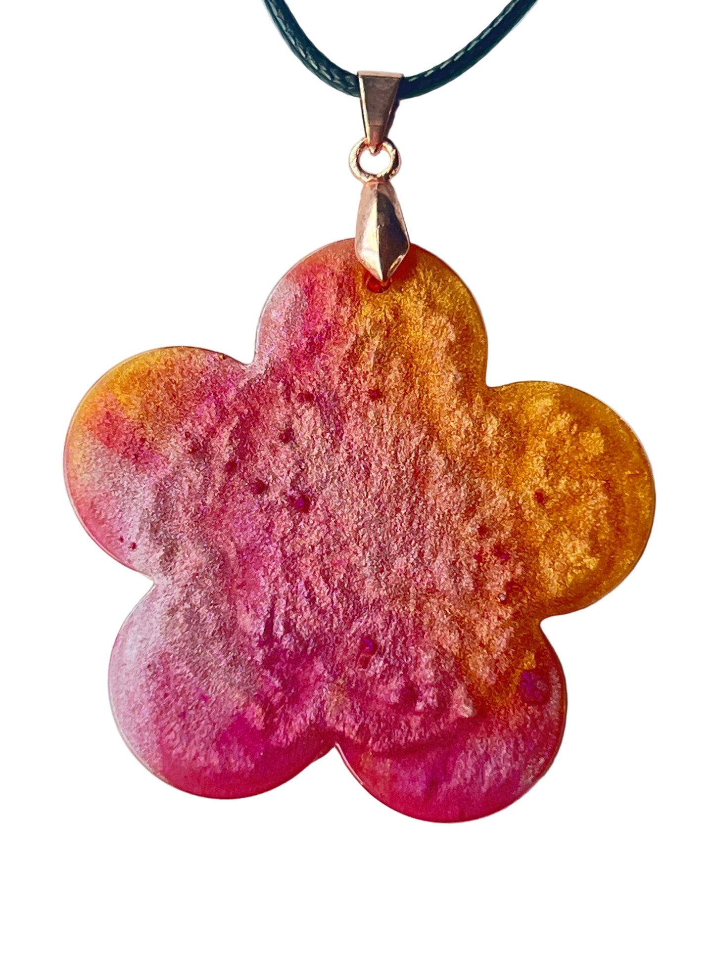 Handcrafted large resin five-petal flower pendant with vivid saturated magenta and hot pink center fading through peachy-coral into warm translucent amber-gold outer petal edges with fine botanical surface texture throughout, suspended from a black braided cord with a rose gold bail.