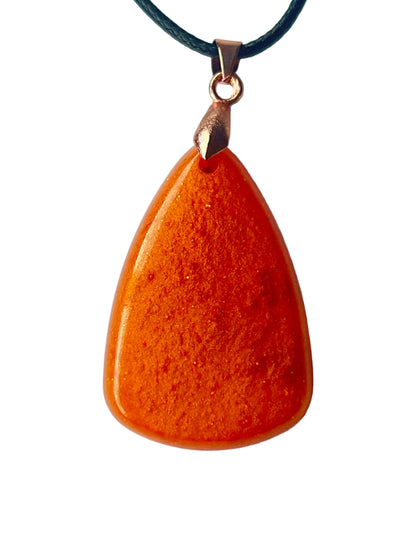 Handcrafted deep opaque carnelian orange resin teardrop pendant with ultra-fine gold and amber shimmer throughout and a high-gloss deeply domed cabochon finish, suspended from a black braided cord with a rose gold bail.