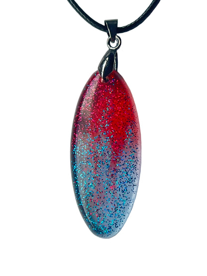 Handcrafted resin elongated marquise pendant with vivid translucent crimson upper field densely filled with magenta-red and pink glitter fading through mauve-purple into cool silver-lavender lower field with dense electric teal and blue glitter, suspended from a black braided cord with a gunmetal bail.