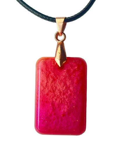 Handcrafted rich opaque coral-red resin rounded rectangle pendant with deep shifting magenta shimmer throughout and scattered fine gold glitter, suspended from a black braided cord with a rose gold bail.