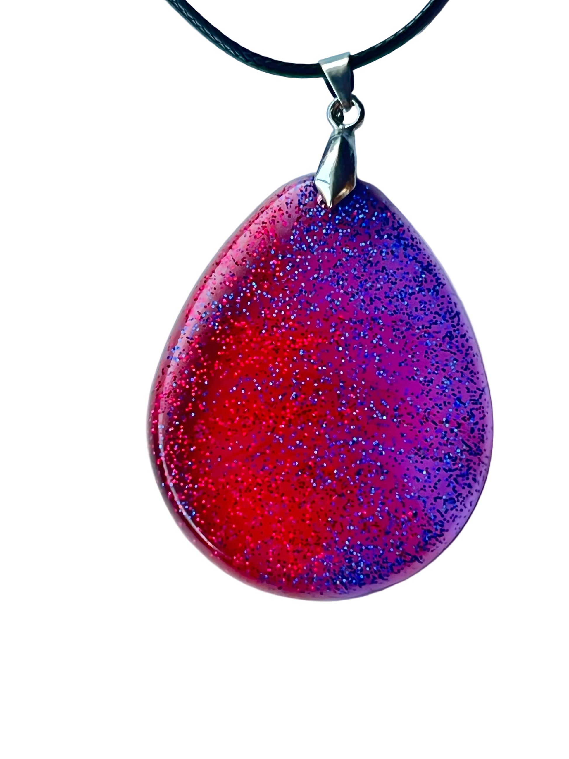 Handcrafted large resin teardrop pendant with vivid translucent crimson-red and electric violet fields meeting in a dynamic diagonal magenta transition, densely filled with ultra-fine red and blue-violet glitter throughout, suspended from a black braided cord with a silver-toned bail.