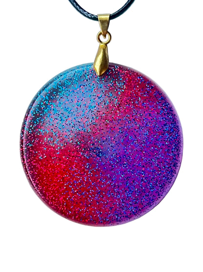 Handcrafted large resin circle pendant with vivid translucent crimson, electric teal, and deep violet-blue fields swirling together with extraordinarily dense ultra-fine glitter throughout in red, teal, and blue-violet, suspended from a black braided cord with a gold-toned bail.