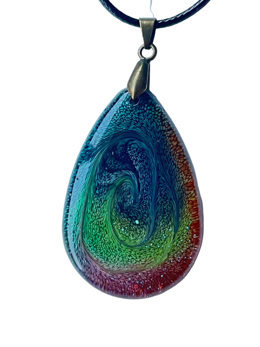 Handcrafted large resin teardrop pendant with a dramatic deep teal and blue-green spiral swirl at center surrounded by a bold rainbow border moving from vivid orange-red through amber to rich magenta-purple with fine cellular texture throughout, suspended from a black braided cord with an antiqued brass bail.