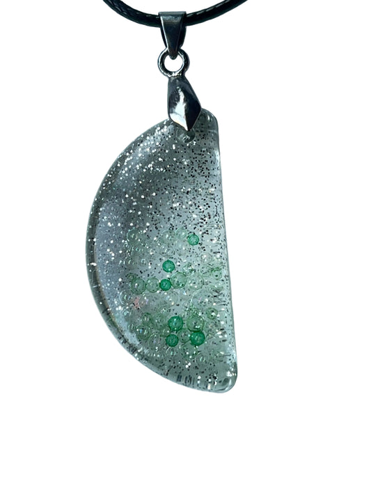 Handcrafted clear crystal resin half-moon pendant with extraordinarily dense ultra-fine silver glitter throughout and two organic clusters of bright emerald-green micro-bubbles floating at varying depths, suspended from a black braided cord with a silver-toned bail.

Next one whenever you're ready! 🌙✨