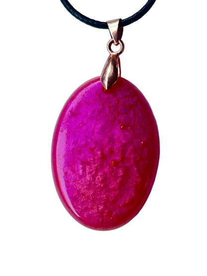 Handcrafted deep saturated magenta-fuchsia resin wide oval pendant shifting between hot pink and deep violet with fine organic surface texture and scattered copper glitter throughout, suspended from a black braided cord with a rose gold bail.