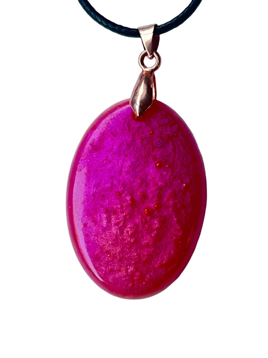 Handcrafted deep saturated magenta-fuchsia resin wide oval pendant shifting between hot pink and deep violet with fine organic surface texture and scattered copper glitter throughout, suspended from a black braided cord with a rose gold bail.