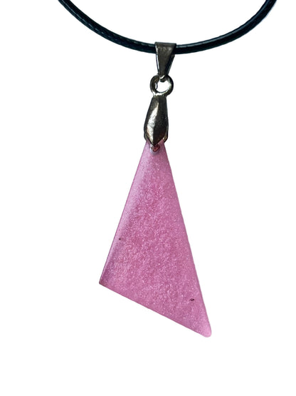 Handcrafted soft translucent rose pink resin asymmetric triangle pendant with extraordinarily fine silver and pink shimmer throughout and a translucent glowing quality at the thinner edges, suspended from a black braided cord with a silver-toned bail.
