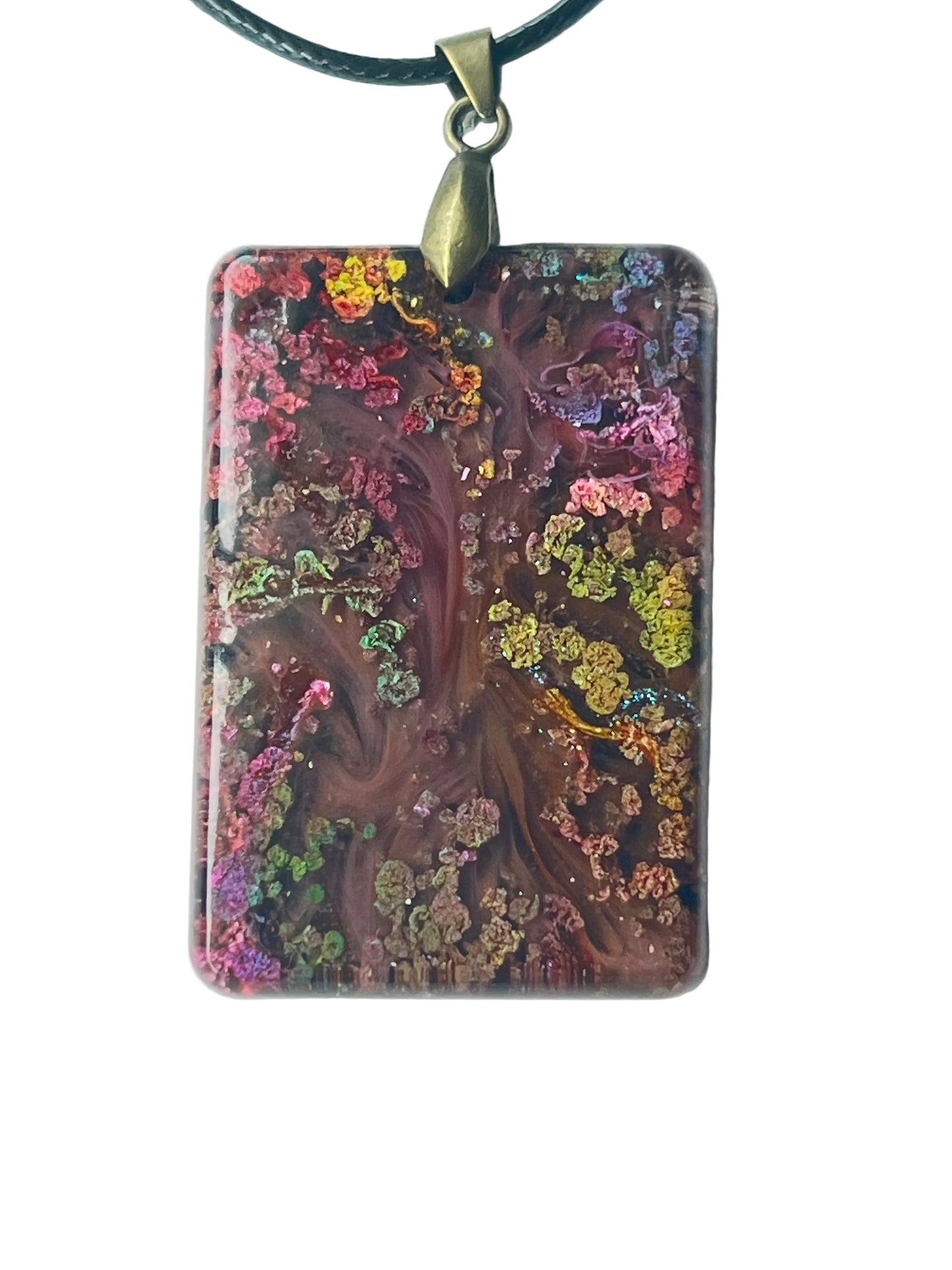 Handcrafted large resin rounded rectangle pendant with deep swirling mahogany and wine-brown organic center formations surrounded by dense iridescent multi-color glitter clusters in vivid pink, chartreuse, gold, violet, and teal throughout, suspended from a black braided cord with an antiqued brass bail.