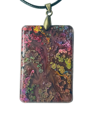 Handcrafted large resin rounded rectangle pendant with deep swirling mahogany and wine-brown organic center formations surrounded by dense iridescent multi-color glitter clusters in vivid pink, chartreuse, gold, violet, and teal throughout, suspended from a black braided cord with an antiqued brass bail.