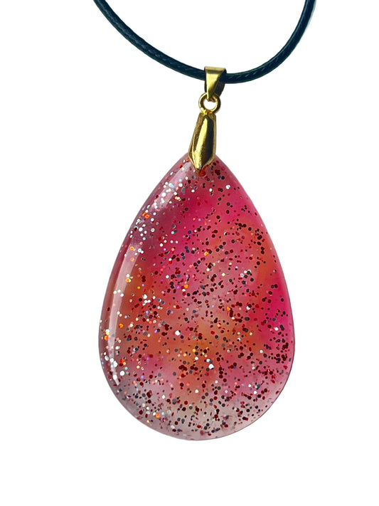 Handcrafted large resin teardrop pendant with soft translucent rose-pink upper field fading into warm peachy-coral lower field with mixed fine red and iridescent silver glitter throughout, suspended from a black braided cord with a gold-toned bail.