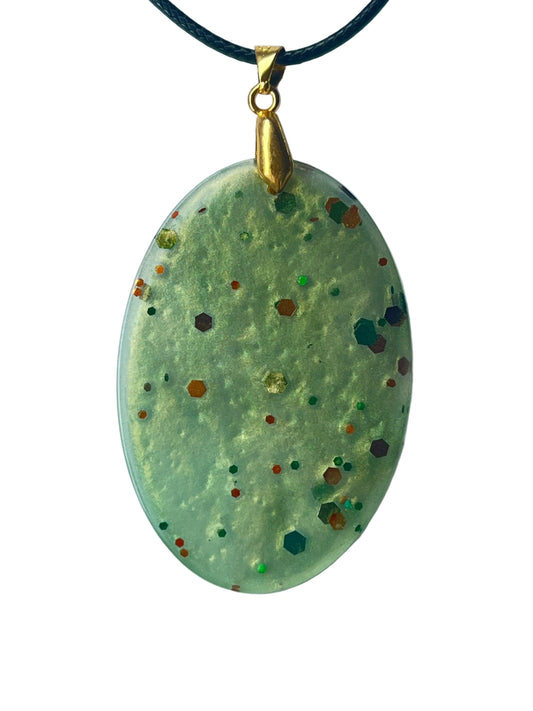 Handcrafted soft milky celadon and pale sage resin large oval pendant with fine gold shimmer throughout and scattered bold hexagonal glitter pieces in copper-orange, teal, forest green, amber, and burgundy at varying depths, suspended from a black braided cord with a gold-toned bail.