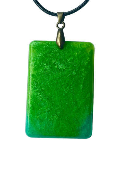 Handcrafted large resin rounded rectangle pendant in fully saturated electric lime and emerald green with fine organic mottled texture throughout and a soft turquoise-blue gradient band along the base, suspended from a black braided cord with an antiqued brass bail.