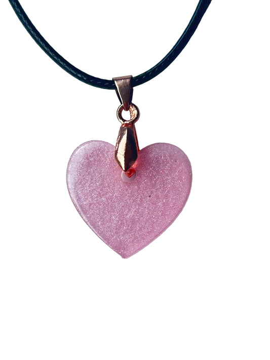 Handcrafted soft translucent dusty rose-pink resin heart pendant with extraordinarily fine silver and pink shimmer throughout and gentle faceted light-catching edges, suspended from a black braided cord with a rose gold bail.