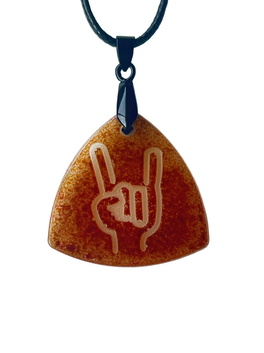 Handcrafted rich warm amber and burnt-orange resin guitar pick-shaped triangle pendant with fine complex texture throughout and a clear raised rock on hand symbol at center, suspended from a black braided cord with a matte black bail.