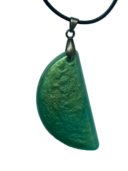 Handcrafted pearlescent green resin half-moon pendant shifting between soft chartreuse and deep grass-green, suspended from a black braided cord with an antiqued brass bail.