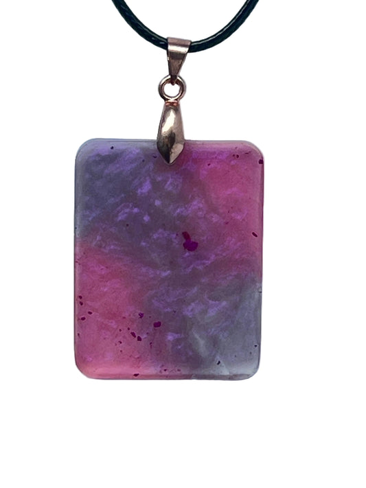 Handcrafted semi-translucent resin rounded rectangle pendant with soft pearlescent mauve and smoky lavender watercolor swirls and scattered deep magenta flecks, suspended from a black braided cord with a rose gold bail.